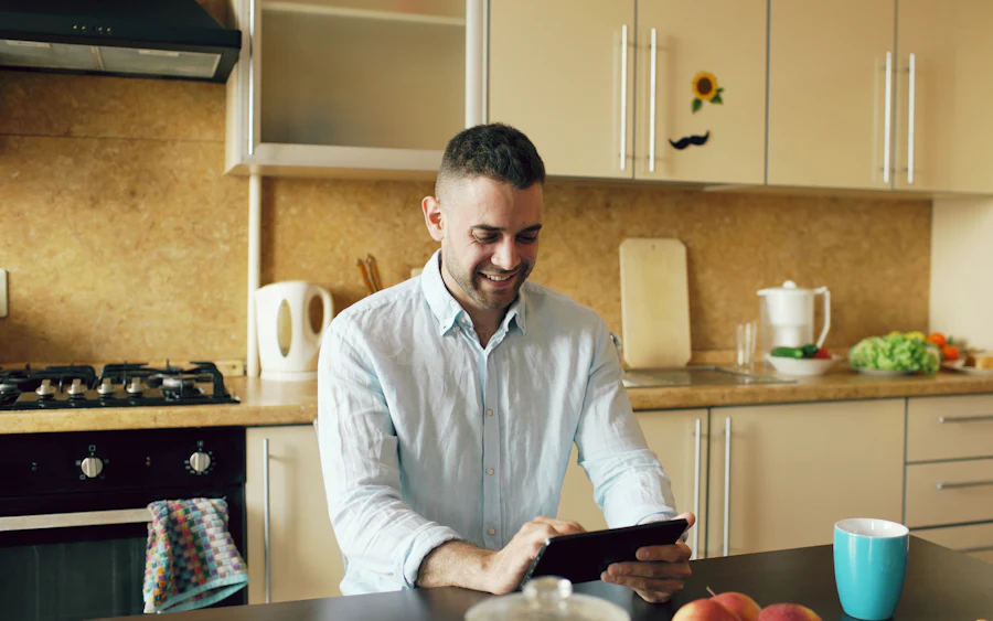 Homem adulto sorrindo enquanto estuda pelo tablet na mesa da cozinha